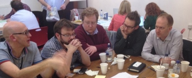 A photo of five men sitting around a table in a breakout session.